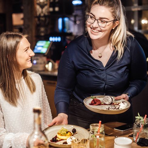 Person an einem Tisch im Restaurant und eine Fachkraft, die ihr essen serviert